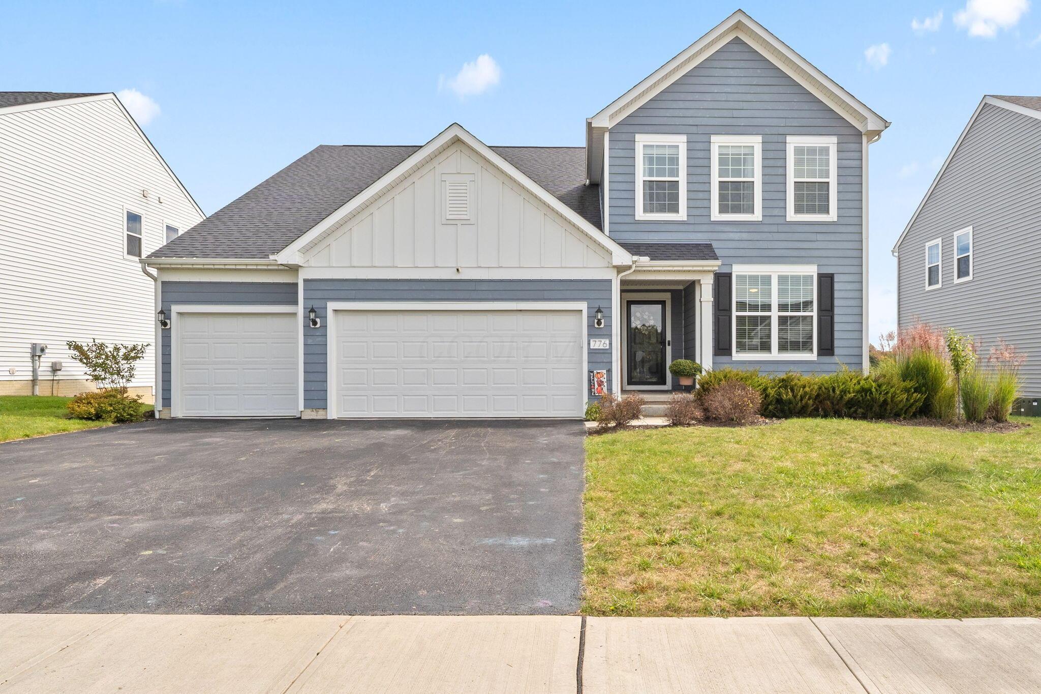 Blue two-story house with white trim, two garage doors, and a wide asphalt driveway.