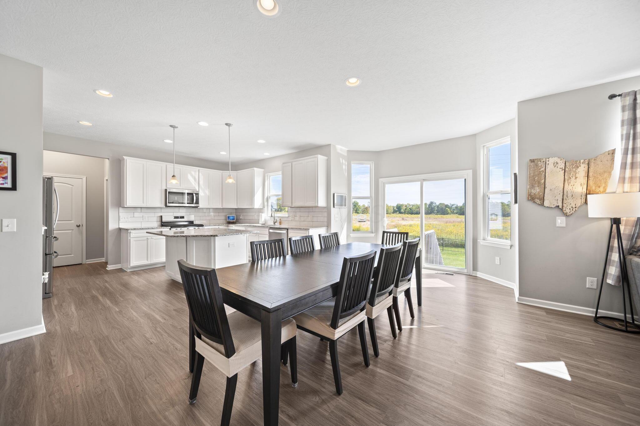 Open-plan kitchen and dining area with a white-cabinet kitchen, dark table, and sliding doors to a grassy field.