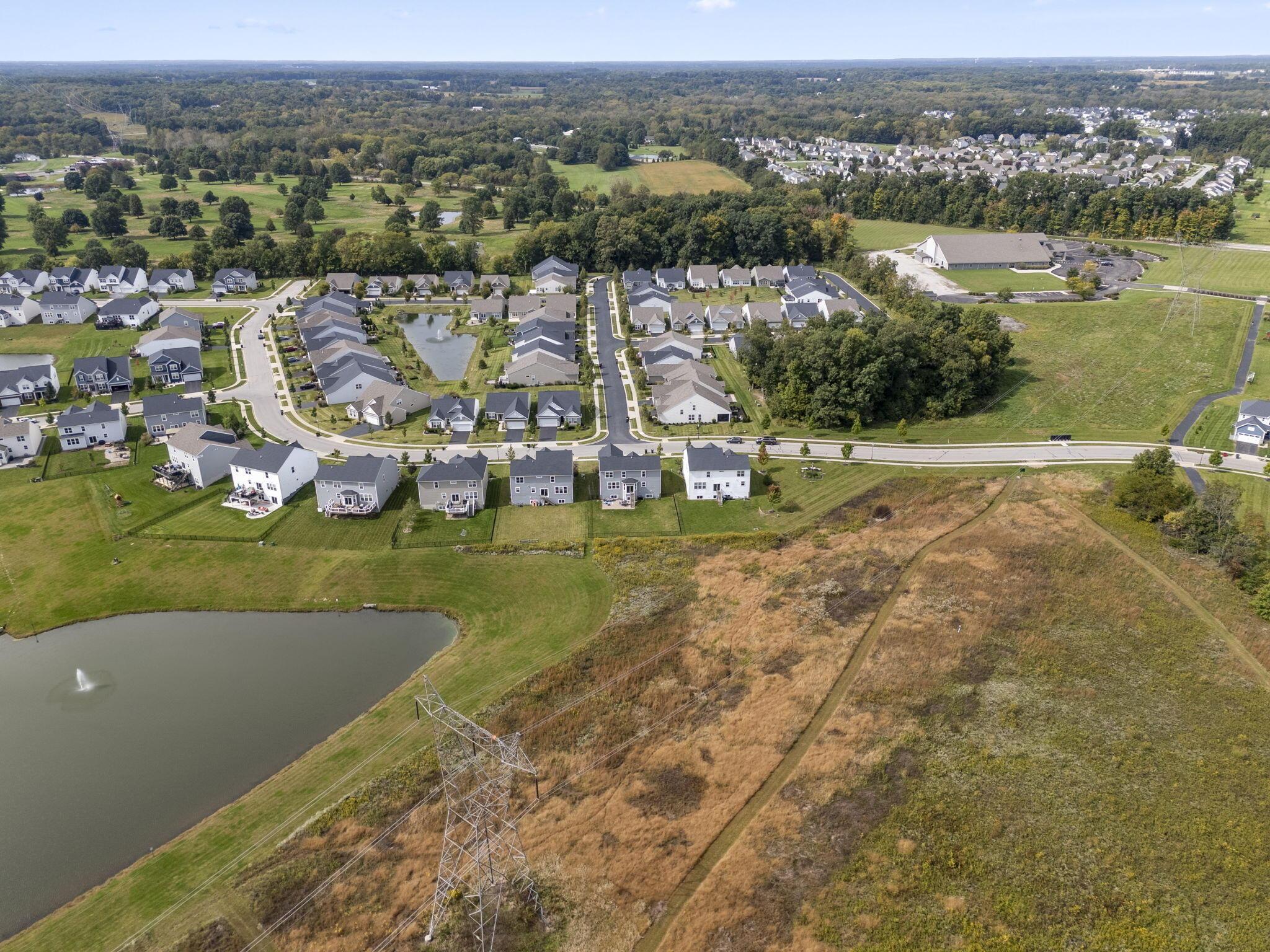 Aerial view of a residential neighborhood with a pond, surrounding fields, and transmission lines.