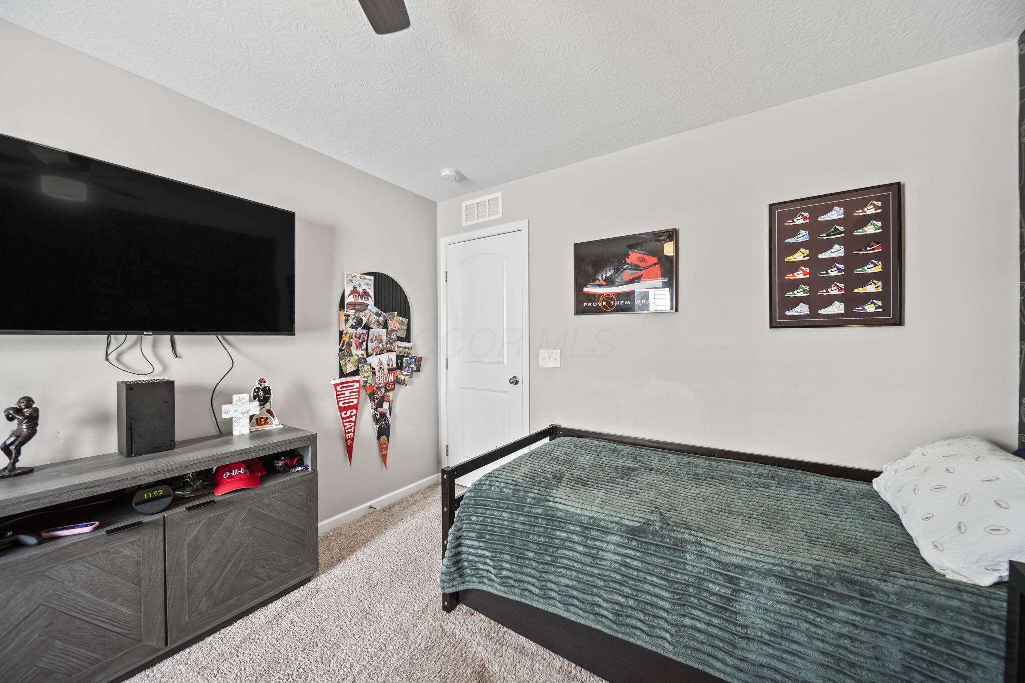 Bedroom with a green-covered bed, large wall-mounted TV, and sports and sneaker memorabilia.