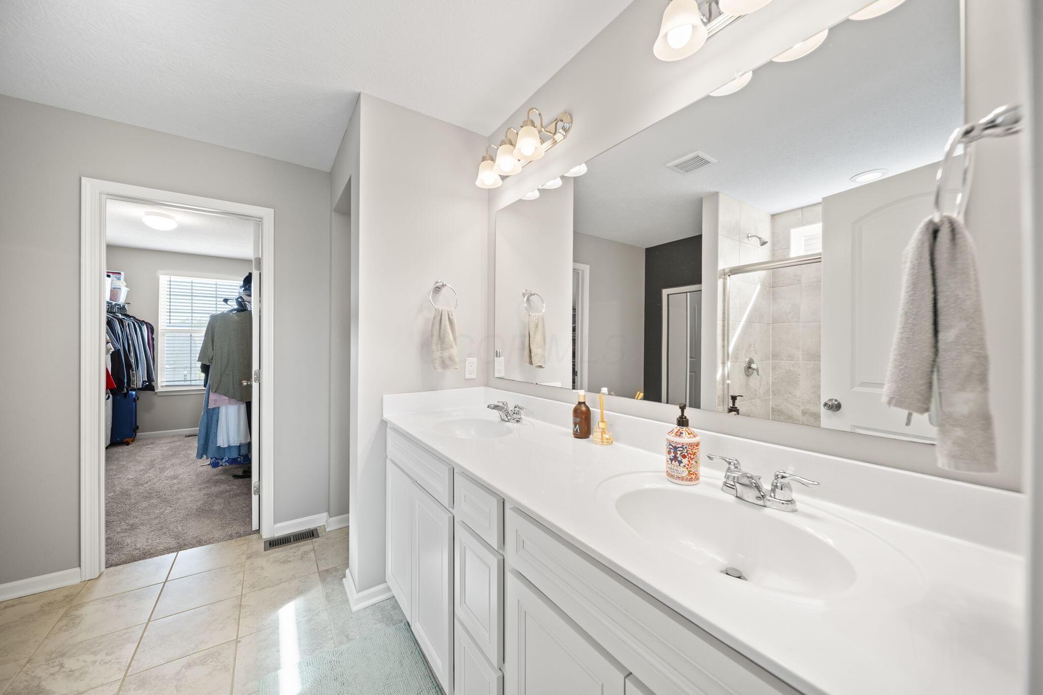 Bathroom with a long double-sink vanity and an adjoining walk-in closet.