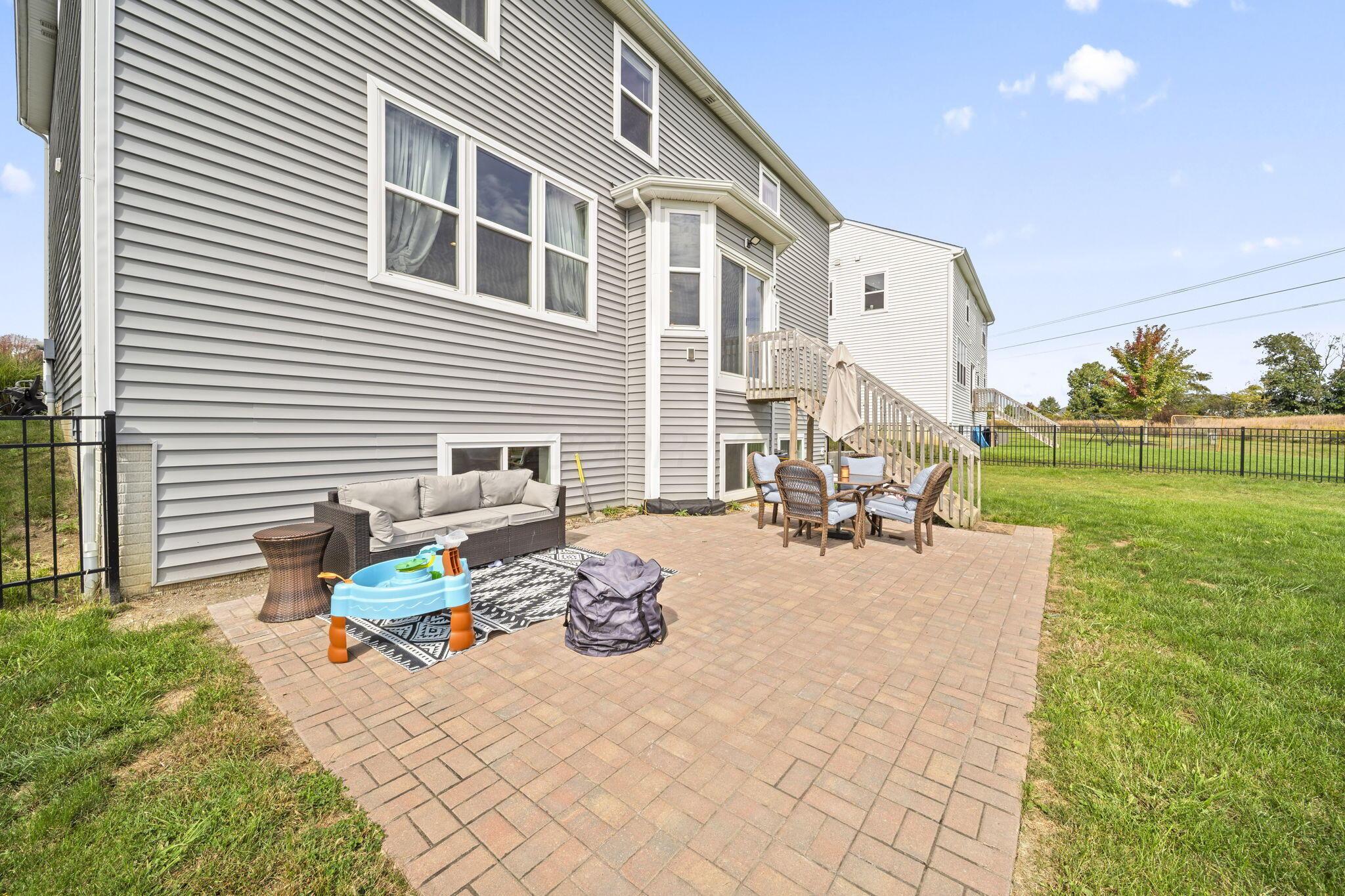 Home’s rear patio with brick pavers, outdoor seating, and stairs to a raised deck.