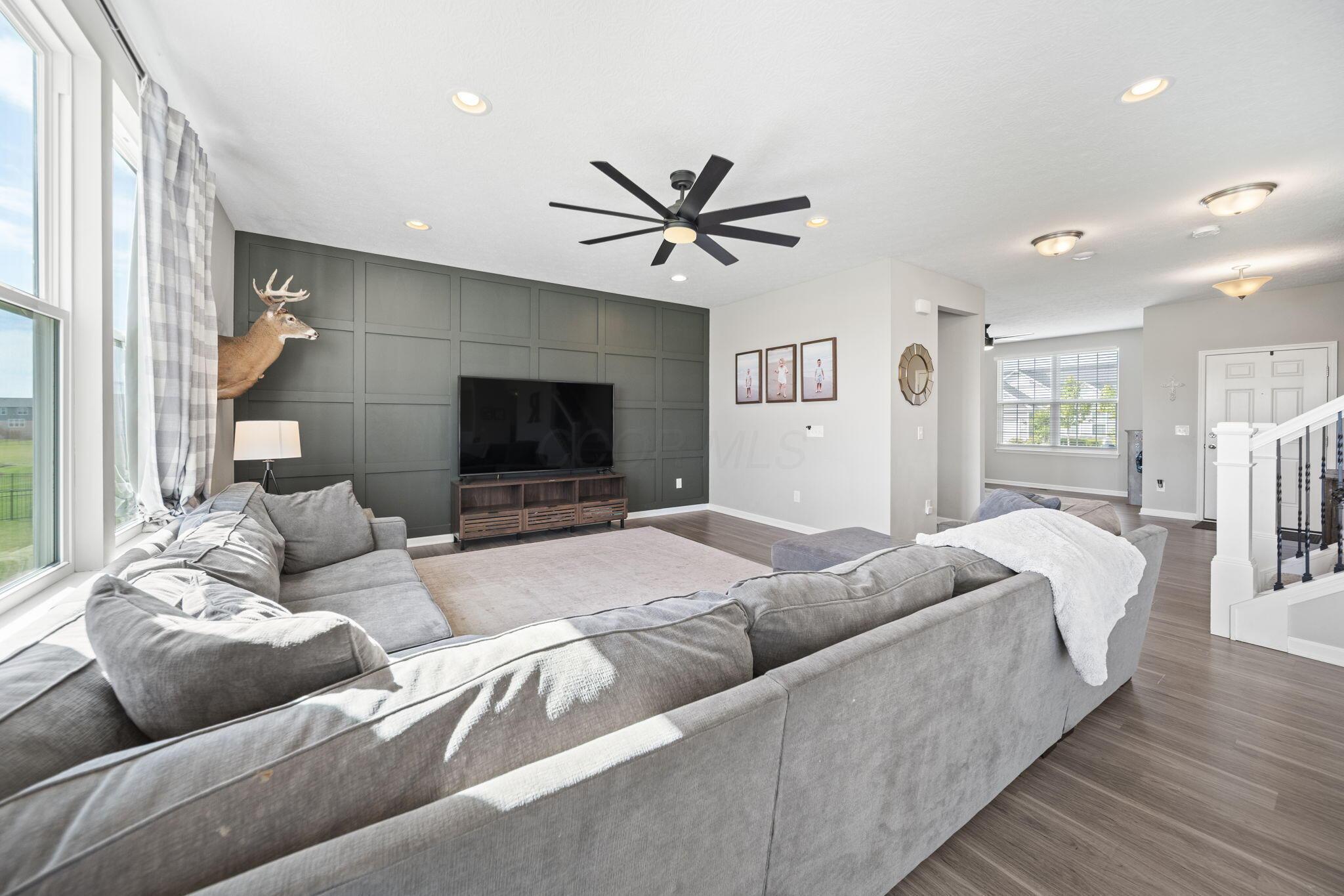 Living room with a gray sectional facing a dark paneled TV wall and mounted deer head.