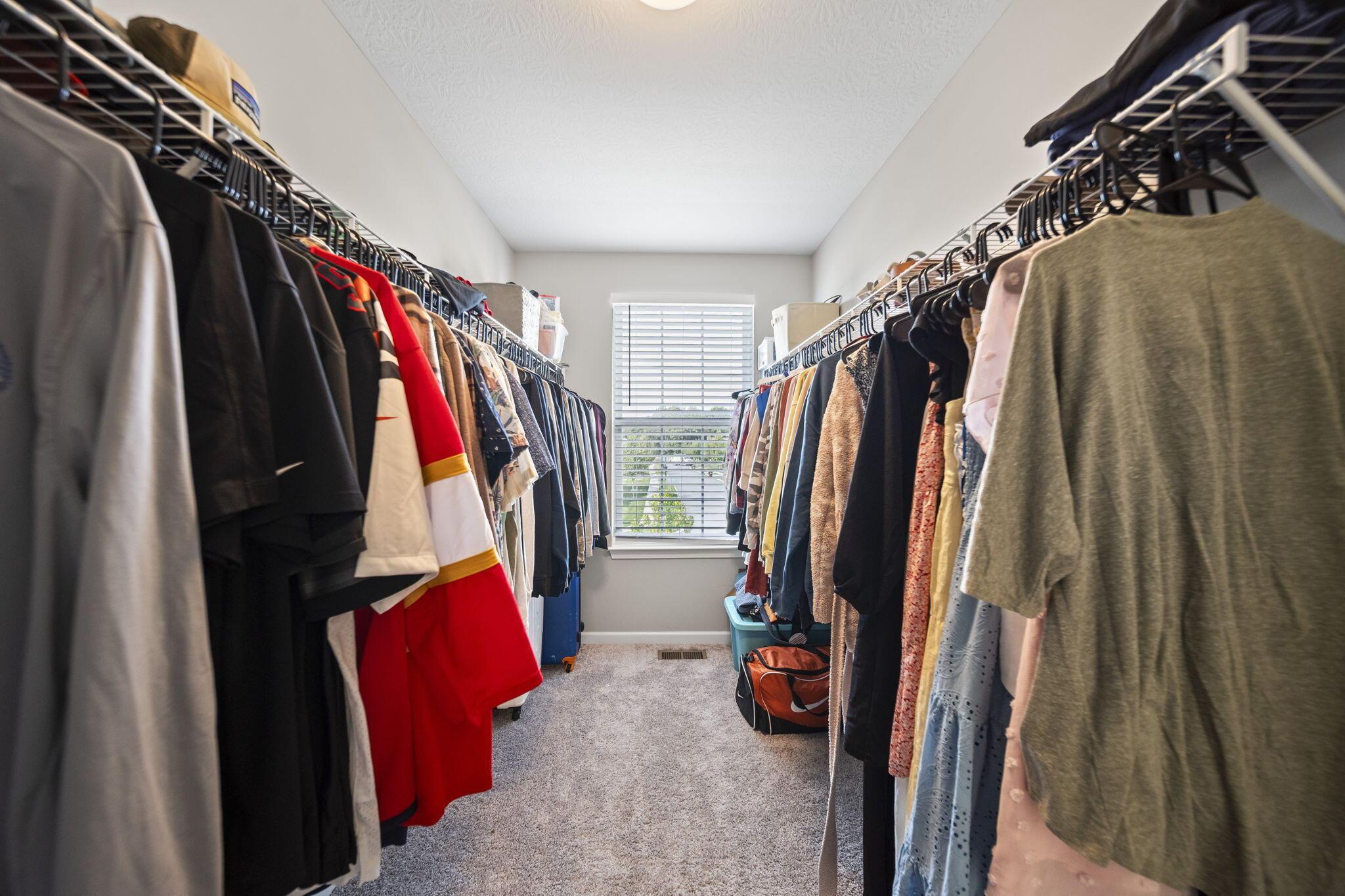 Walk-in closet with clothes on both sides and a window at the far end.