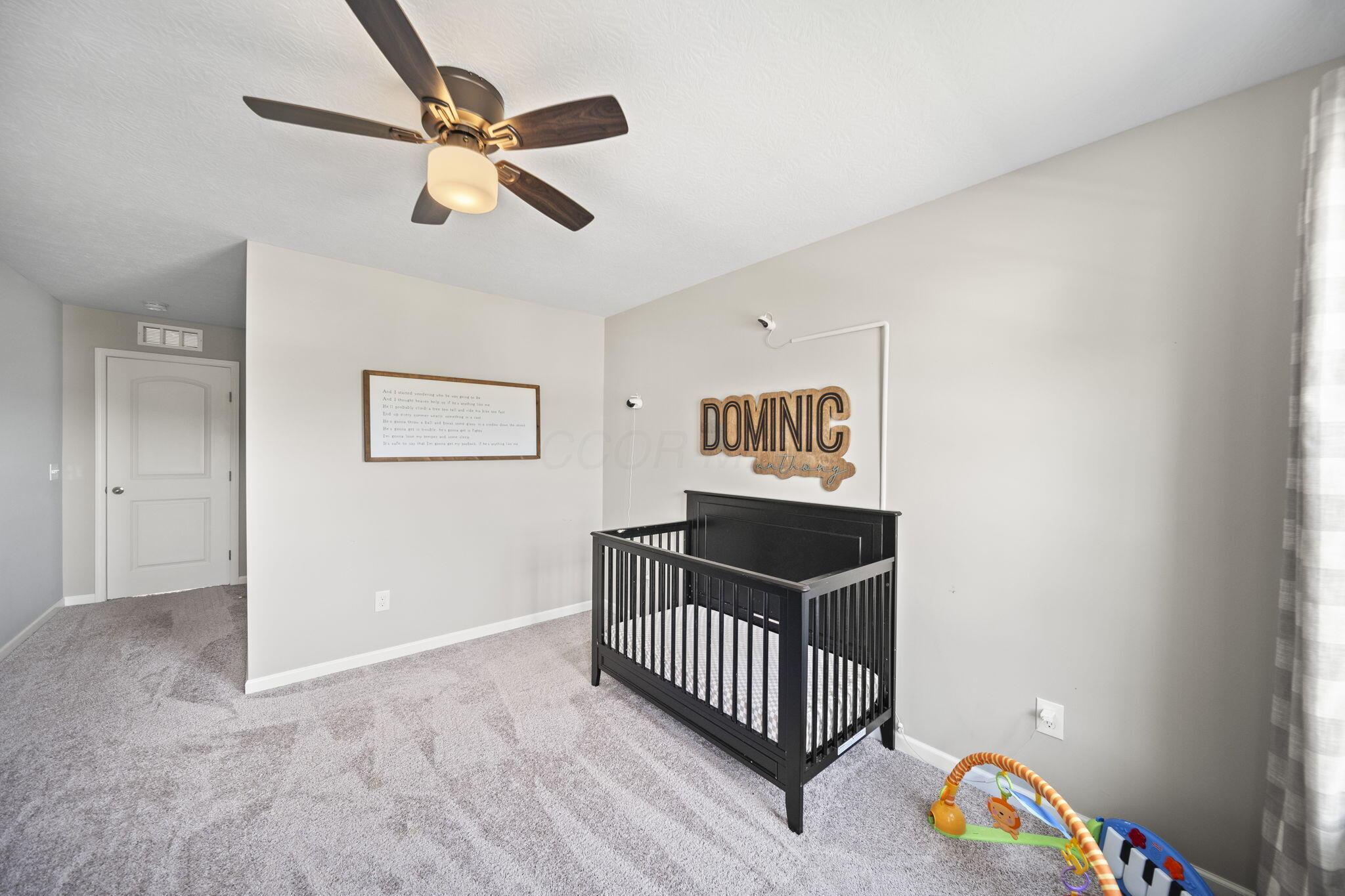Nursery with a black crib beneath a wooden Dominic sign and baby play equipment by the window.