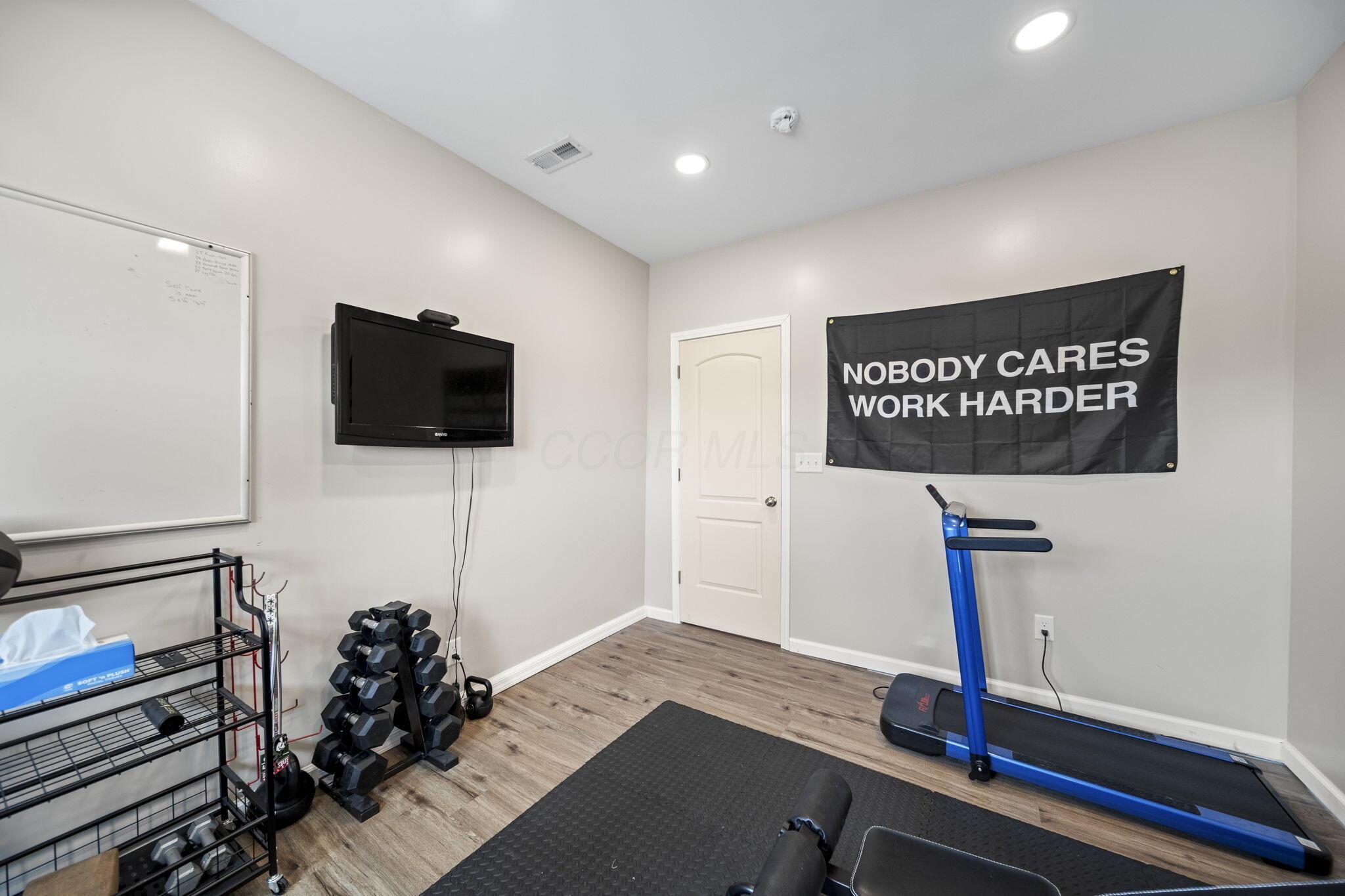 Home gym with a blue treadmill, dumbbell rack, exercise mat, television, and motivational banner.