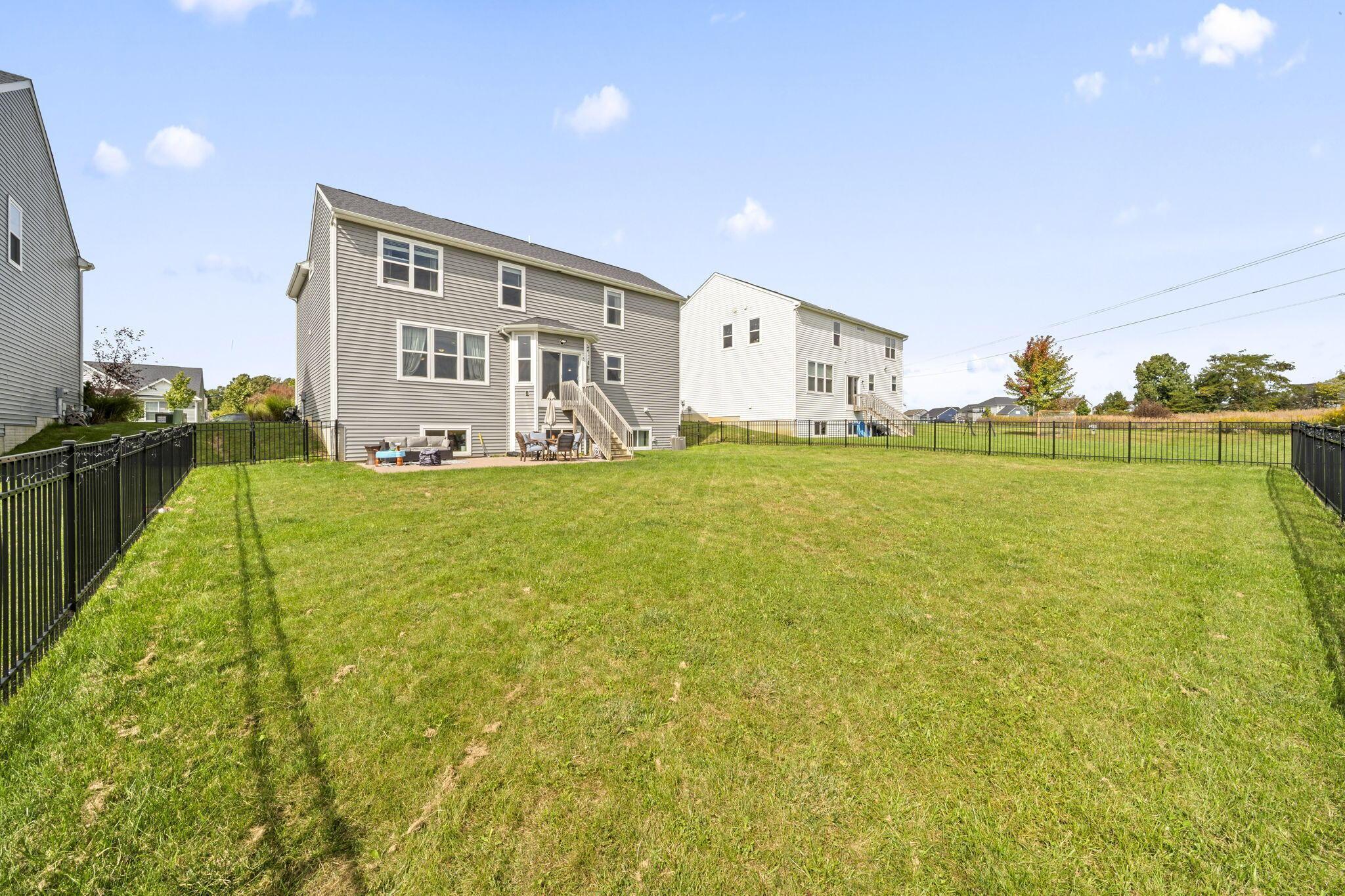 Gray two-story home beyond a spacious fenced backyard, with a raised deck and patio seating.