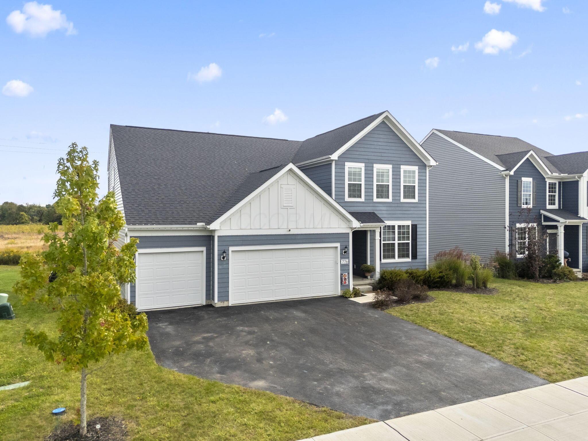 Blue-gray two-story house with white trim, twin garage doors, and a wide driveway.