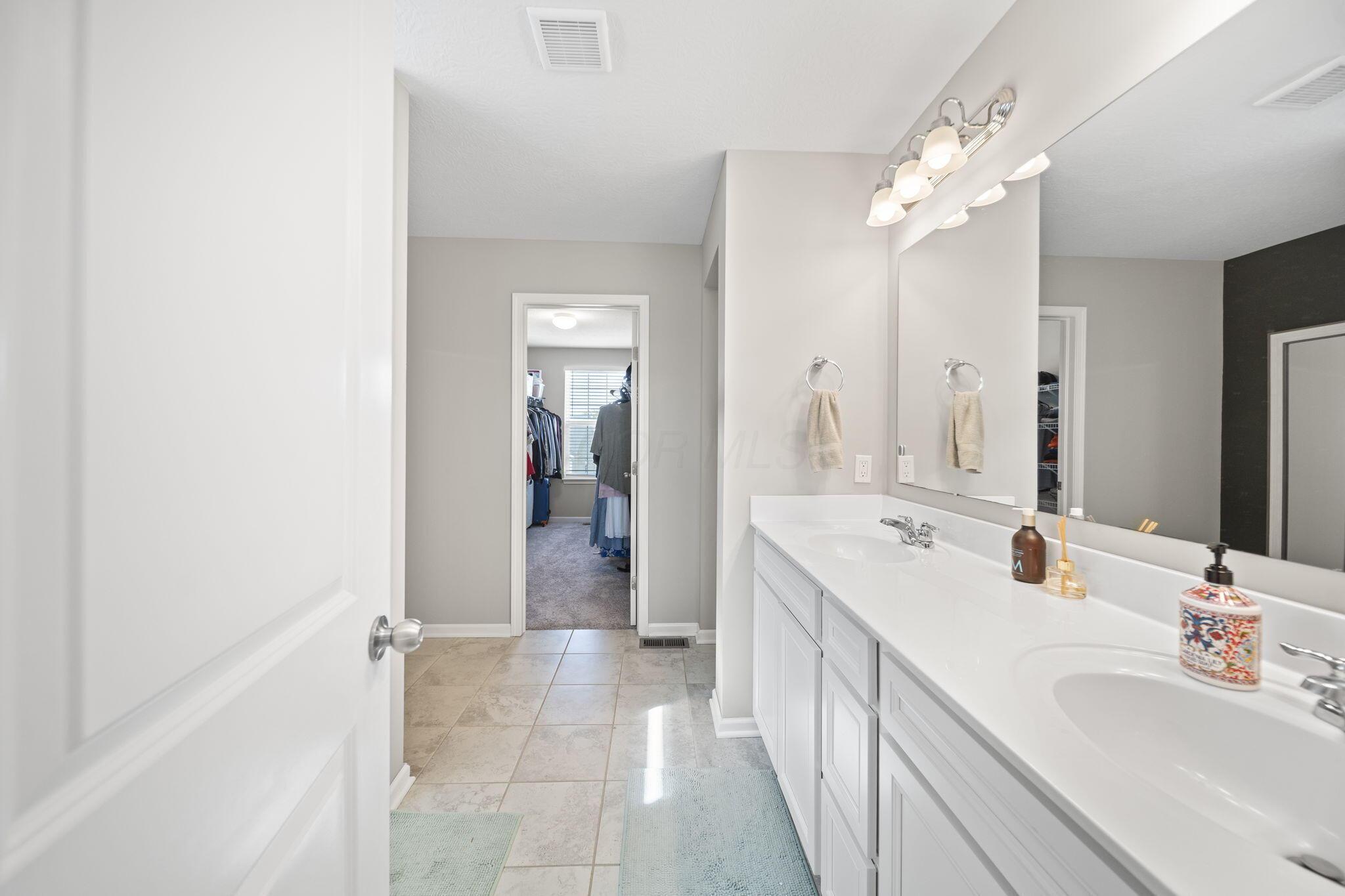 Bathroom with a long double-sink vanity and a walk-in closet visible through the doorway.