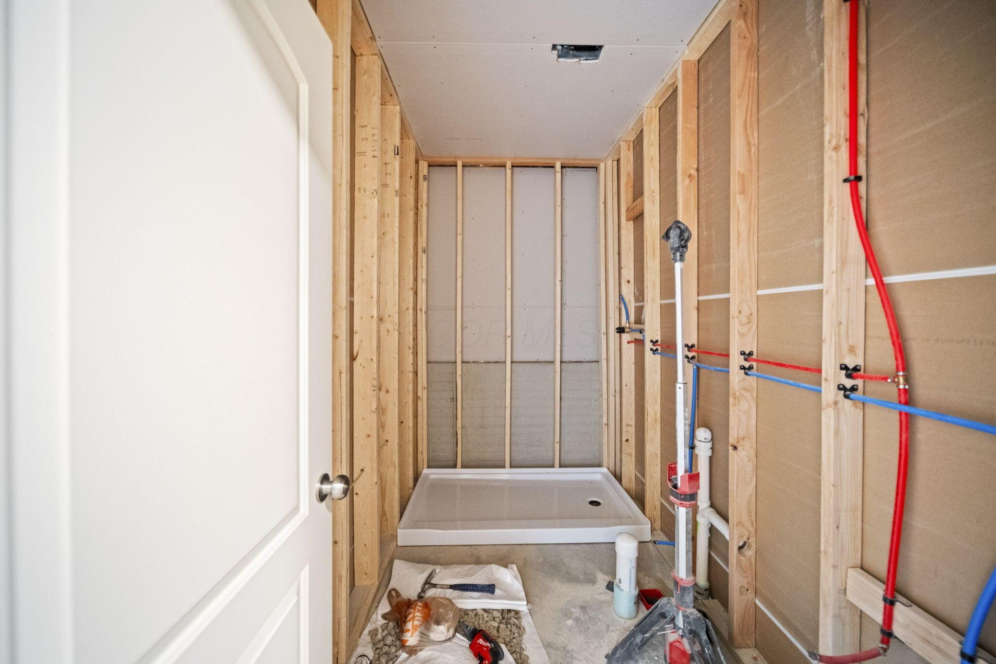 Framed bathroom with exposed plumbing and a shower pan under construction.