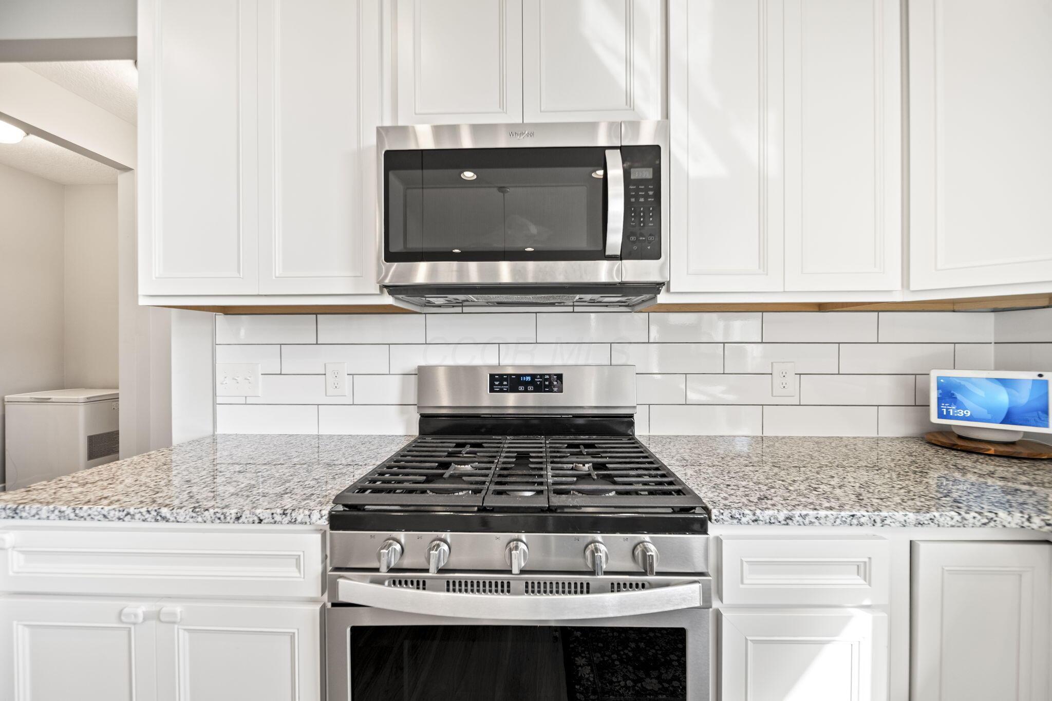 Kitchen with white cabinets, granite counters, and a stainless steel gas range beneath a microwave.