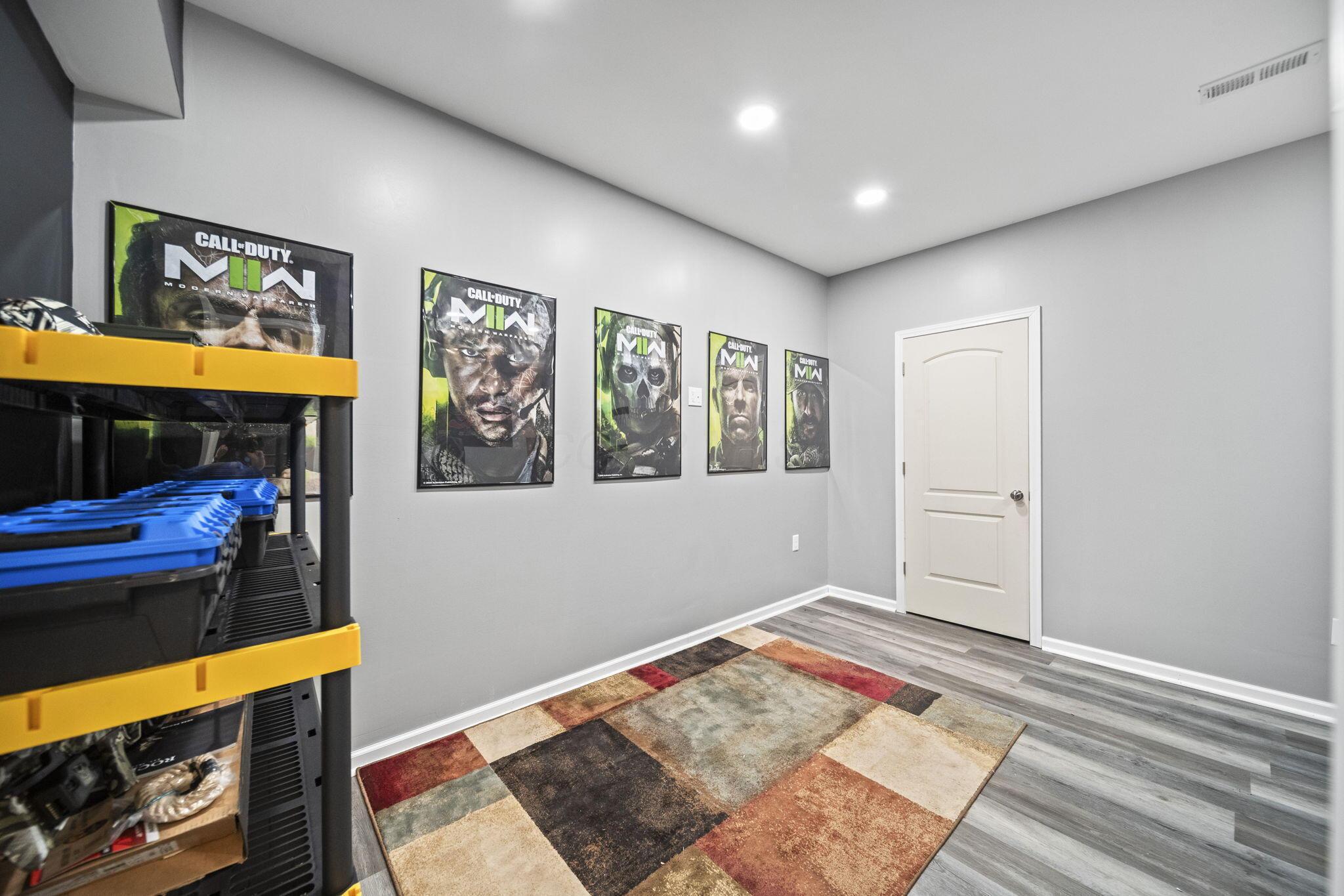 Room with framed Call of Duty posters, gaming equipment shelving, and a multicolored rug.