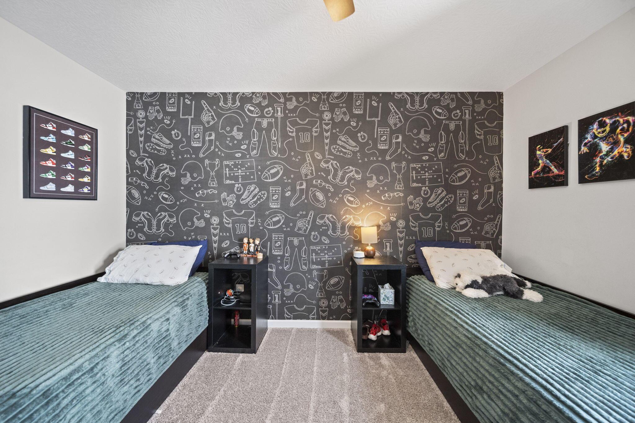 Bedroom with twin teal beds, sports-patterned wallpaper, and framed sports artwork.
