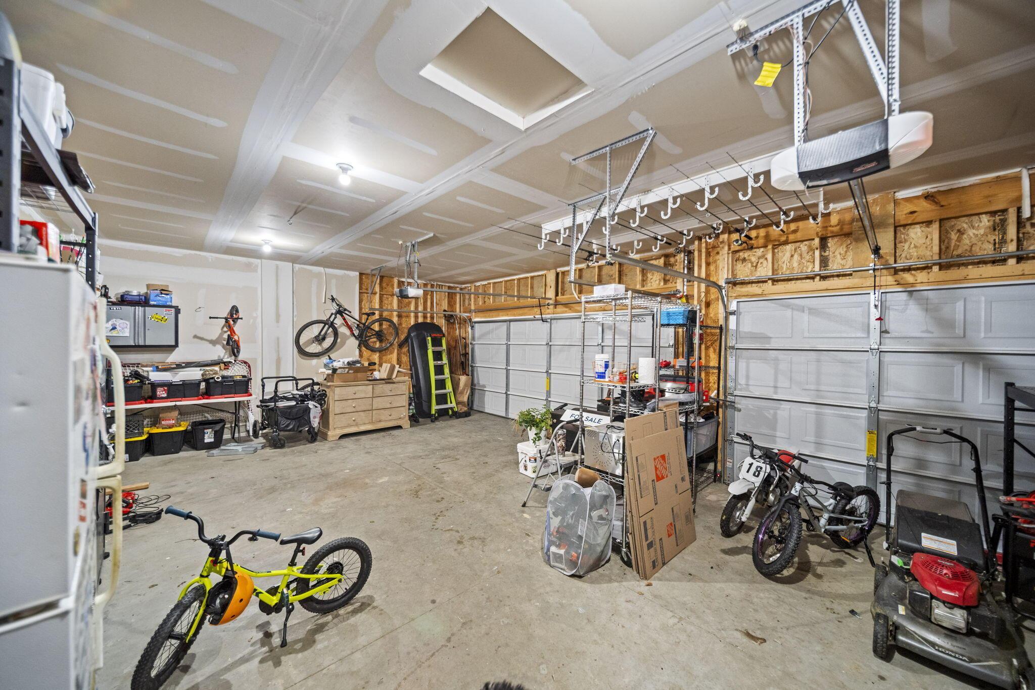 Large garage with two overhead doors, ceiling storage racks, bicycles, and tools.