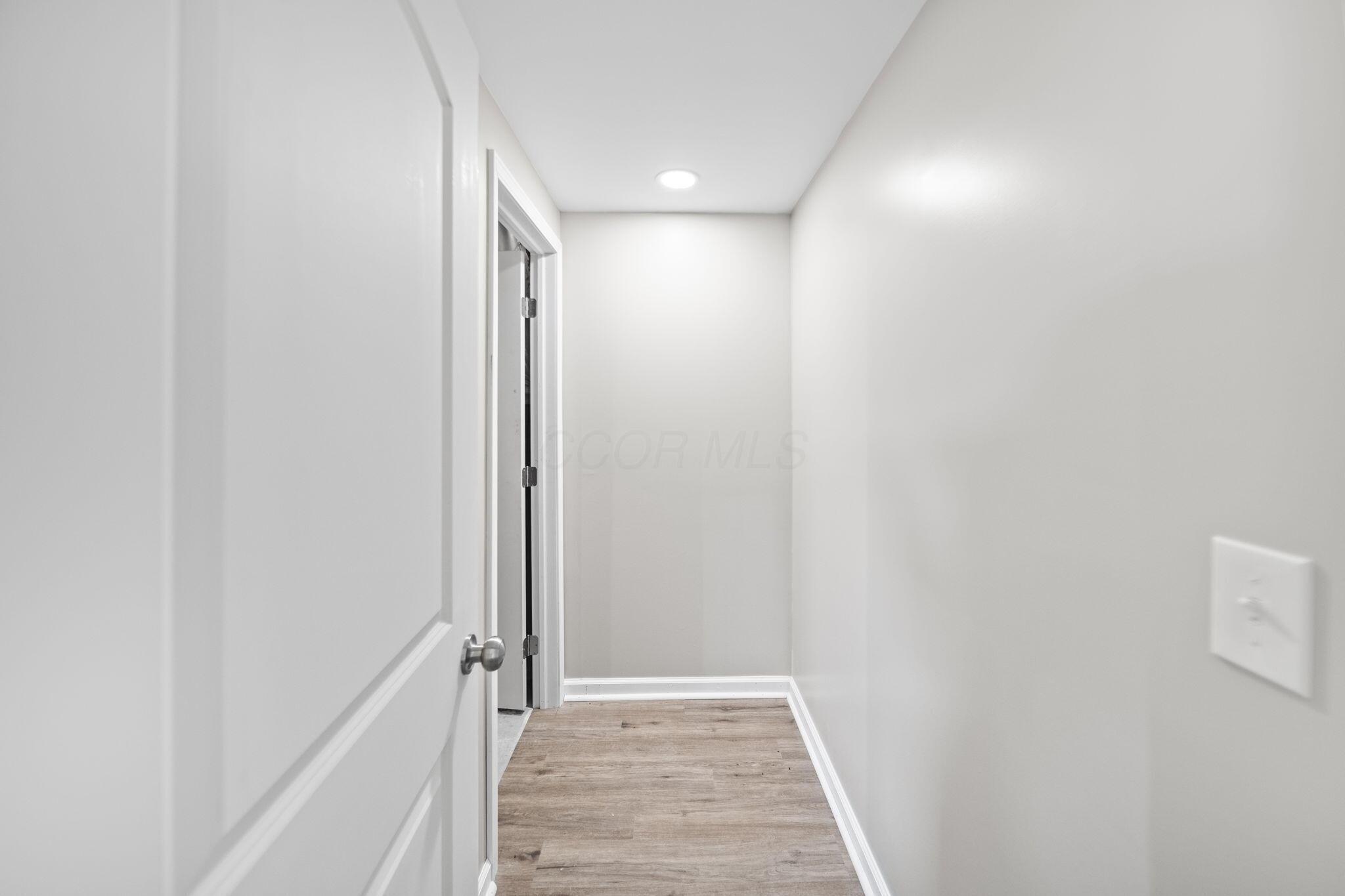 Unfurnished hallway with wood-look flooring, white trim, and an open door in the foreground.