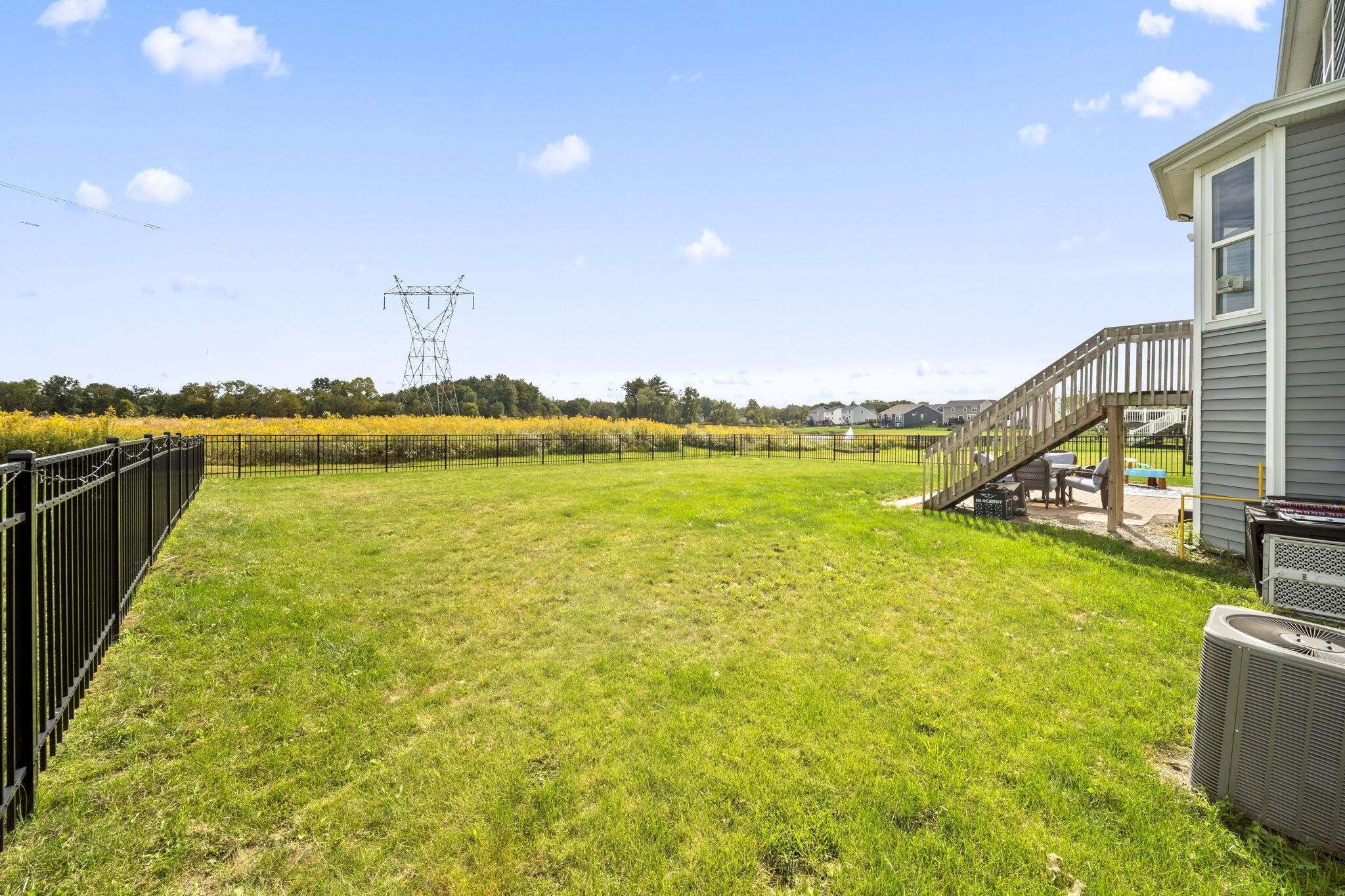 Fenced backyard with a broad lawn, raised deck, and patio seating beside the house.