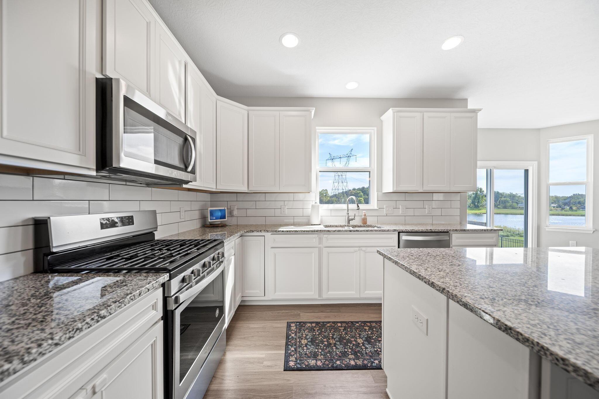 Bright white kitchen with granite counters, a large island, stainless steel appliances, and water views through the windows.