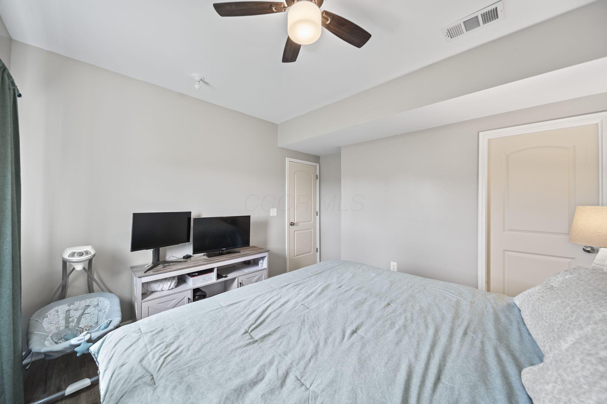 Bedroom with a large bed, two monitors on a console, and a ceiling fan.