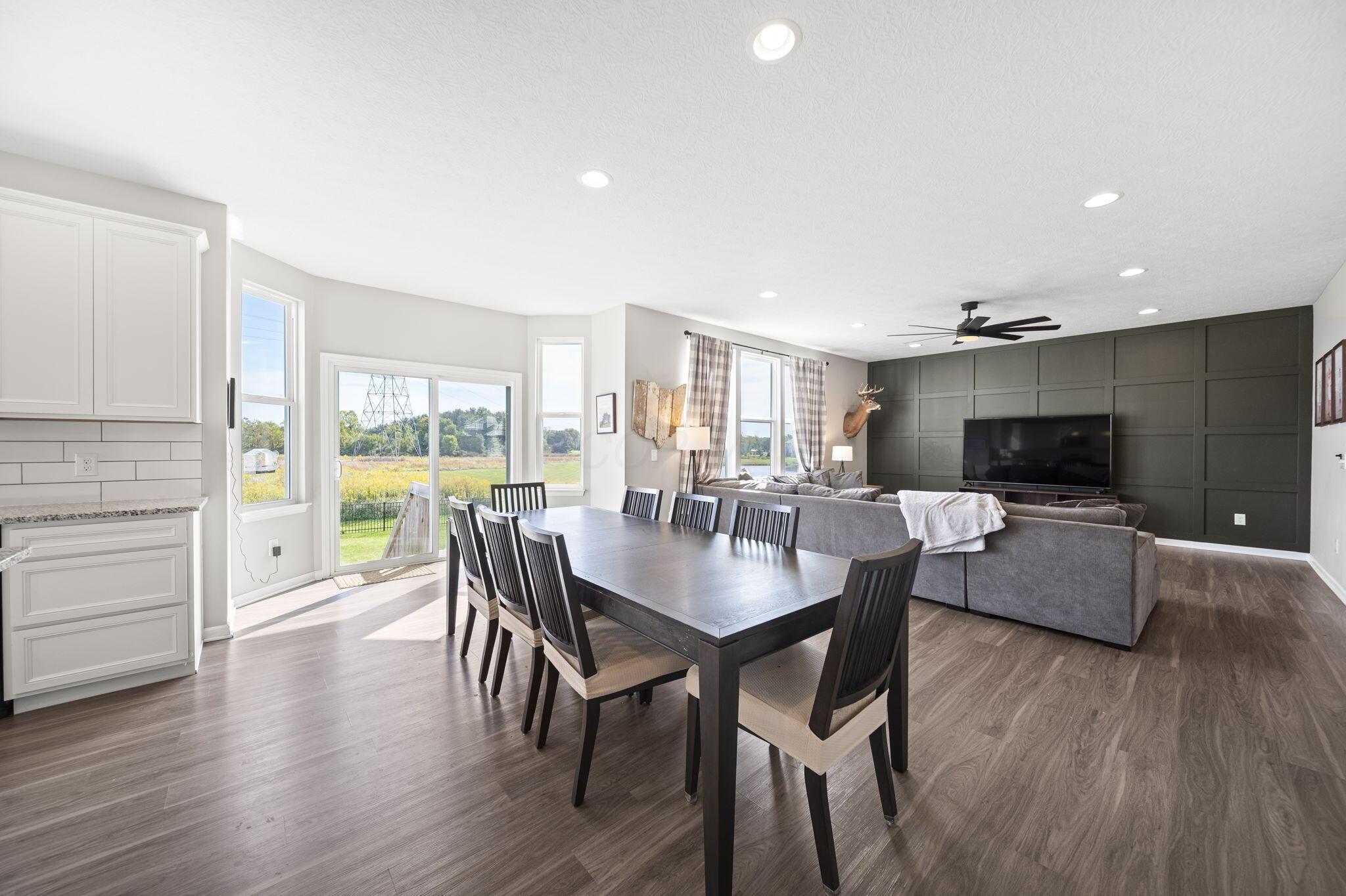 Open-plan dining and living room with a dark dining table, gray sectional, and charcoal paneled TV wall.