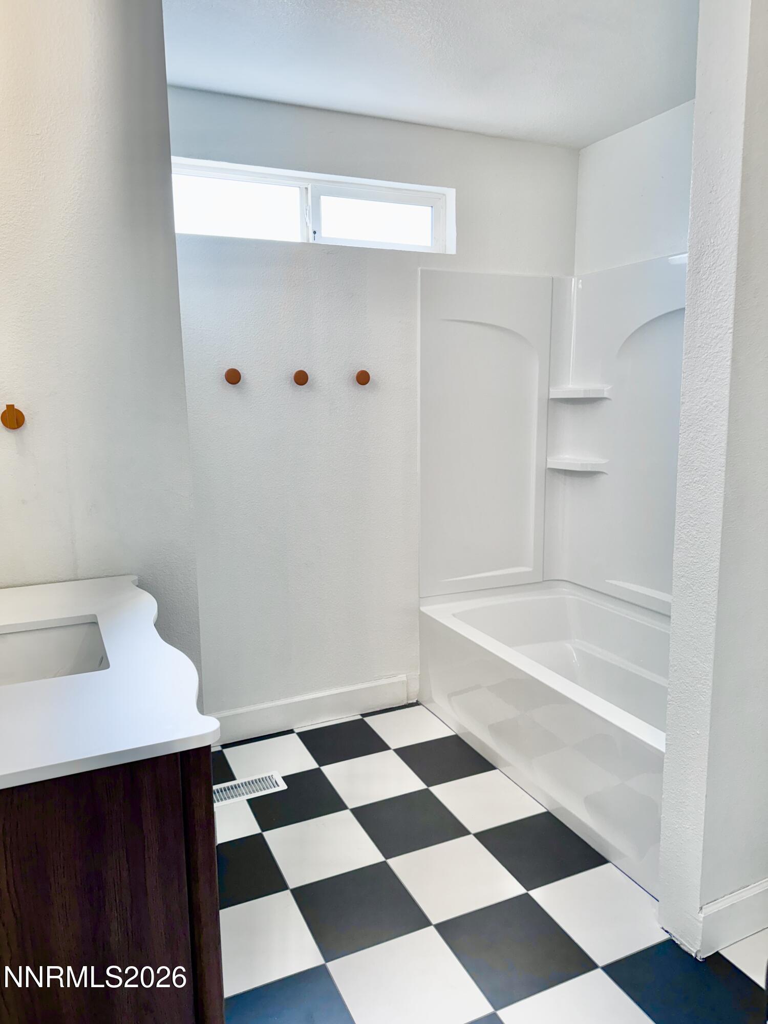 Bathroom with a white tub and shower, checkerboard floor, and dark wood vanity.