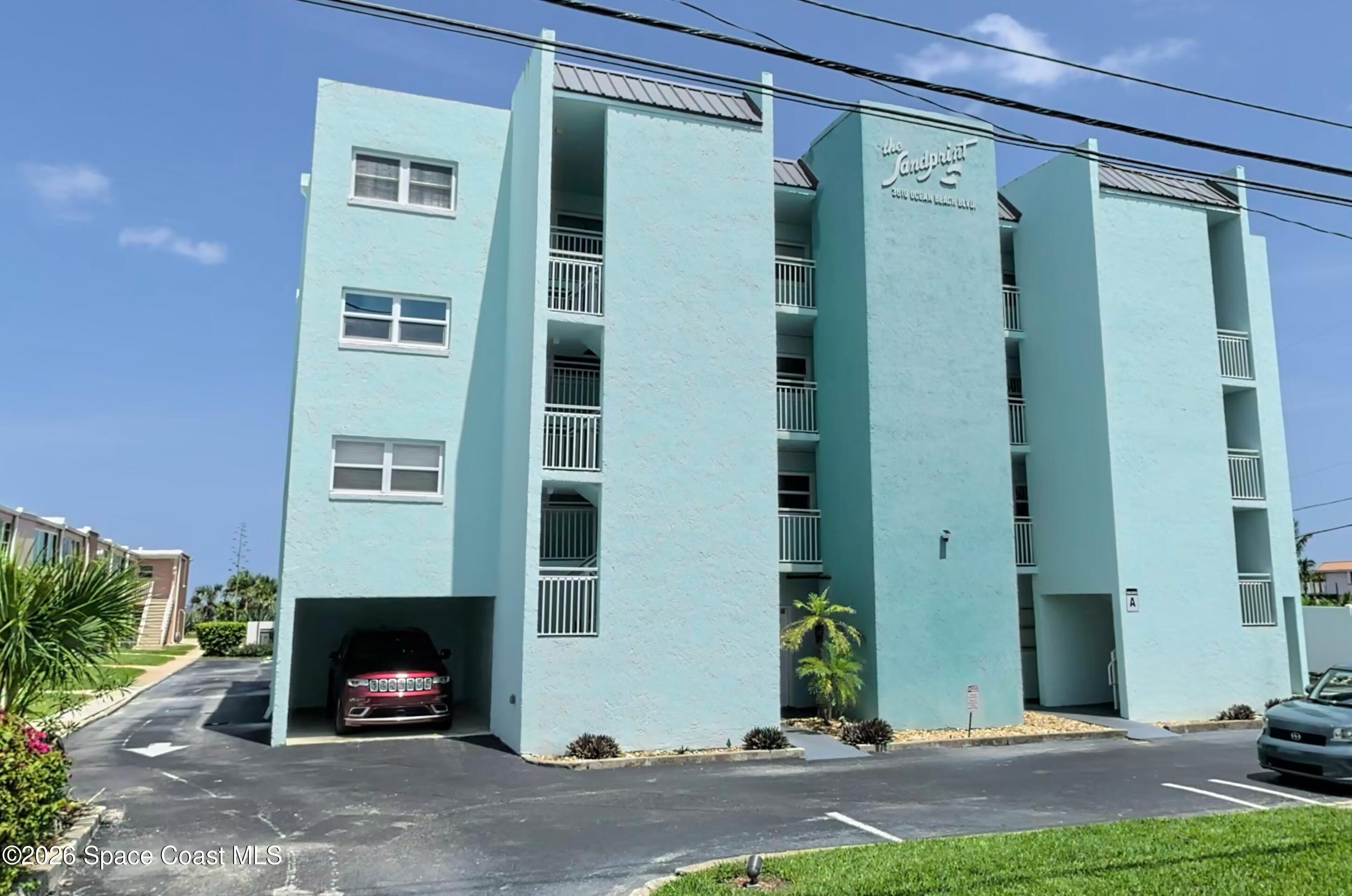 The Sandpiper condominium’s pale aqua exterior with balconies and covered parking.