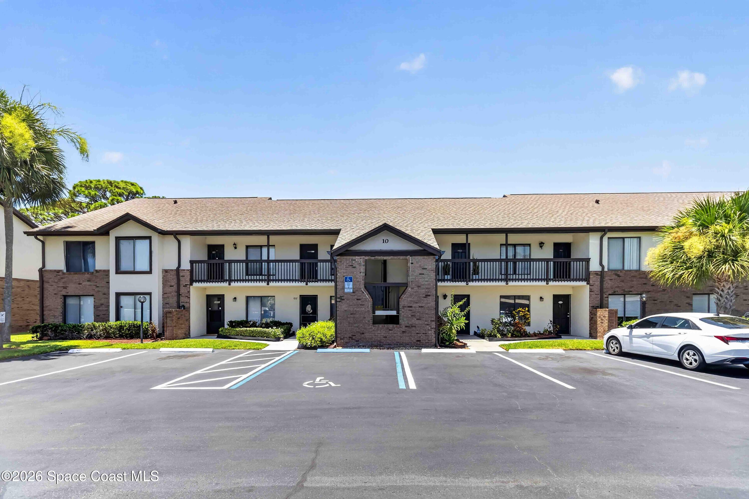 Two-story brick and stucco condominium building with long balconies and accessible parking in front.
