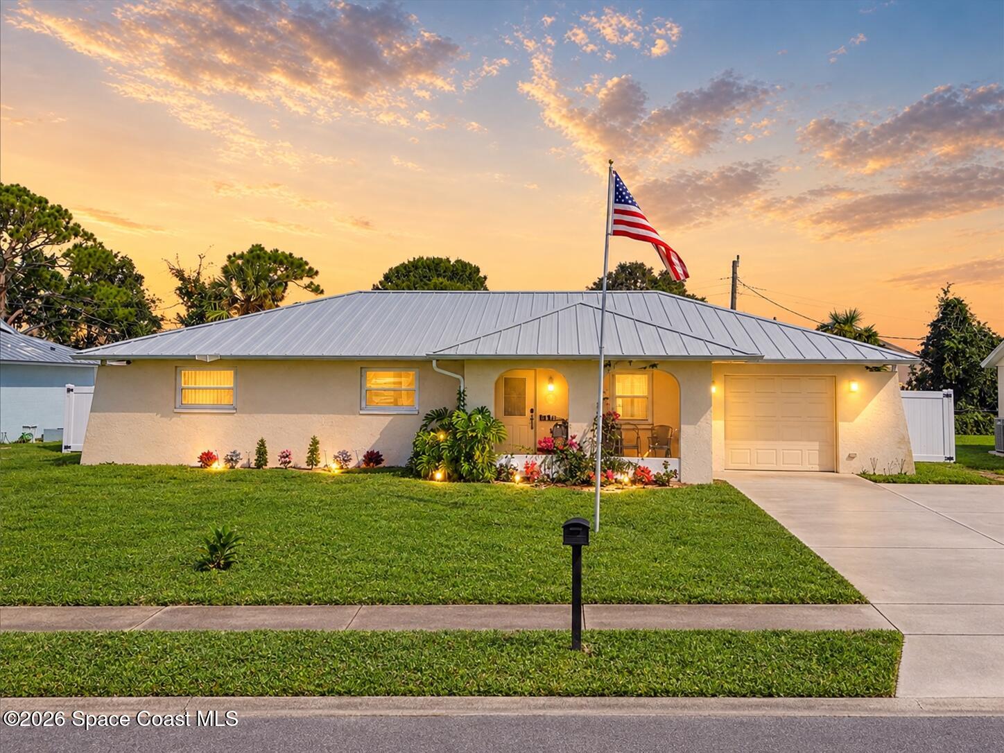 Single-story home with a metal roof, attached garage, and American flag at sunset.