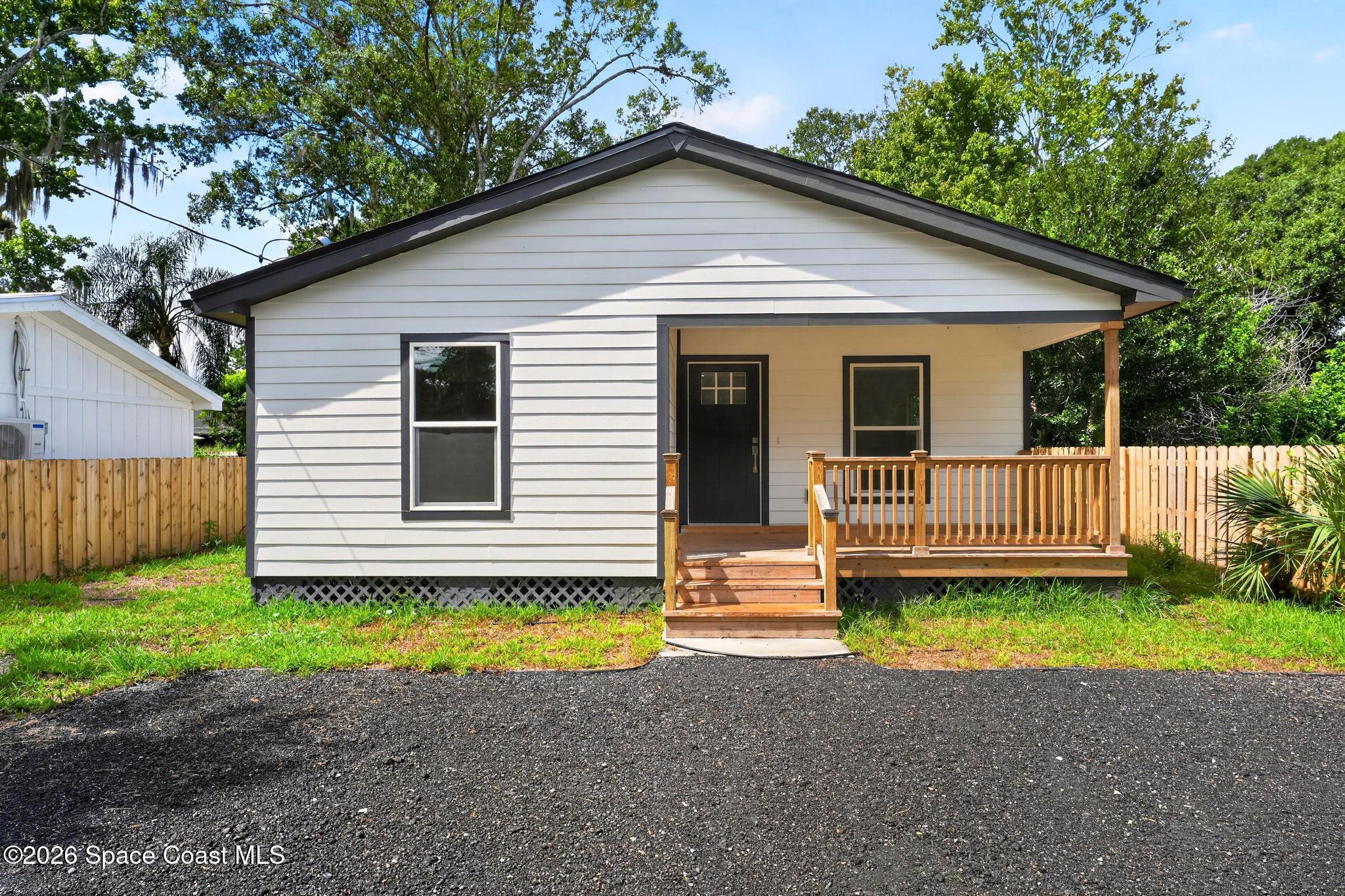 Small white house with a covered wooden porch, front steps, and fenced yard.