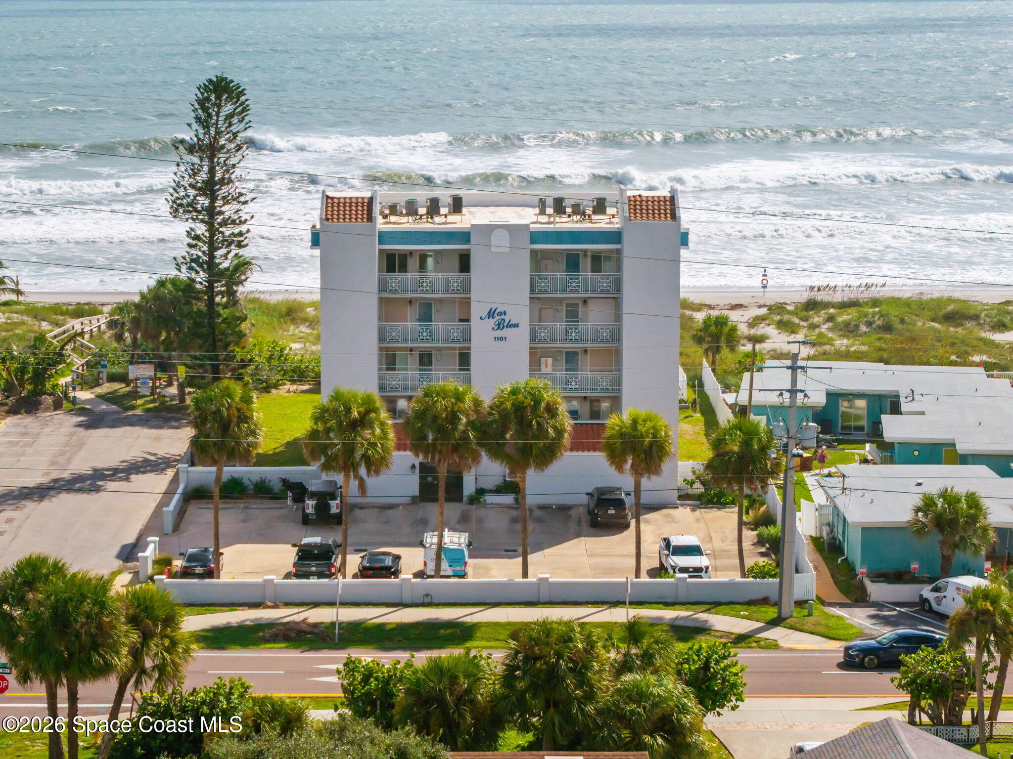 Mar Bleu beachfront condominium with balconies, palm trees, and the ocean behind it.