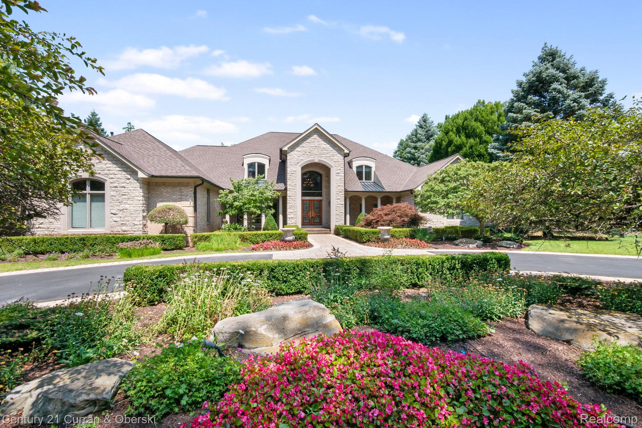 Stone house with an arched entrance, landscaped gardens, and a flower-lined front path.