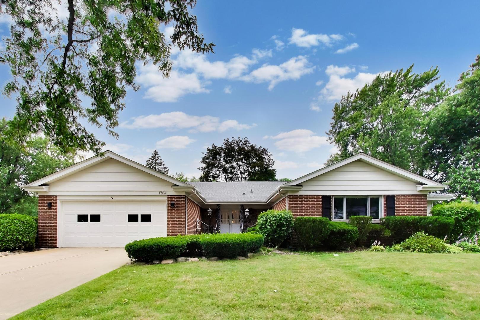 Brick ranch home with an attached two-car garage, trimmed shrubs, and a broad front lawn.