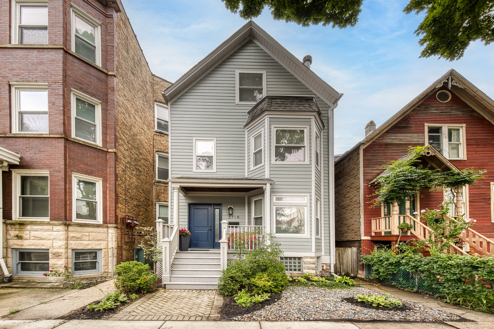 Gray two-story house with a blue front door, white porch steps, and landscaped yard.