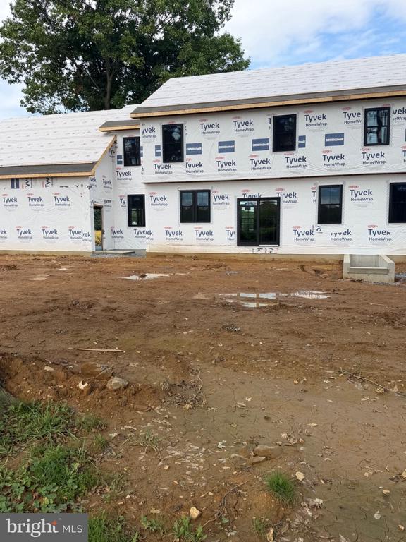 Two-story home under construction, wrapped in Tyvek, with an unfinished dirt yard.