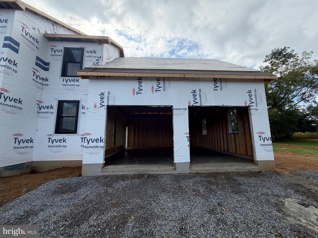 Two-story home under construction with Tyvek wrap and two open garage bays.