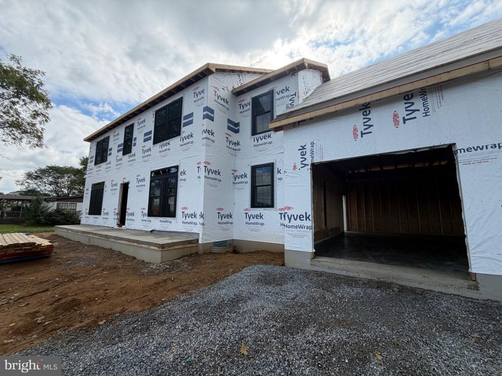 Two-story house under construction, wrapped in Tyvek, with an open garage and unfinished exterior.