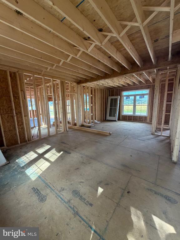 Unfinished interior room with exposed framing, concrete subfloor, and a large sunlit window.
