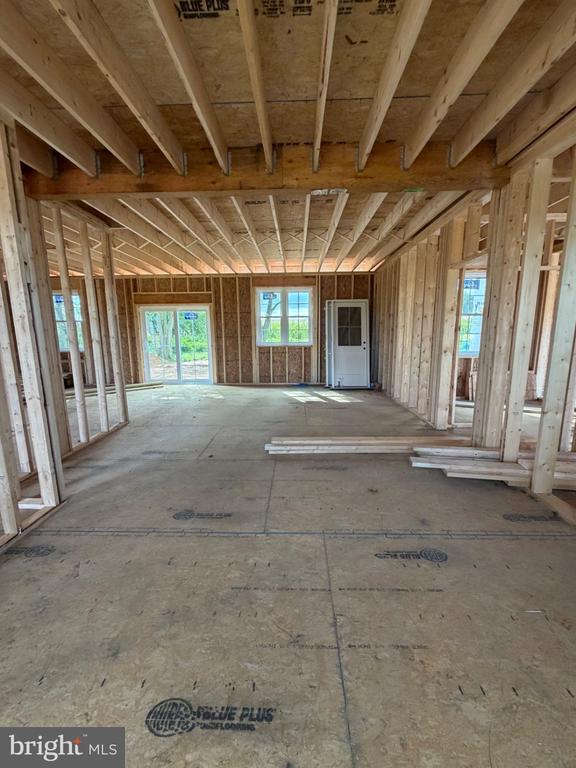 Unfinished home interior with exposed wood framing, concrete floor, and daylight through windows.