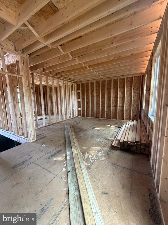 Unfinished interior with exposed wood framing, ceiling joists, and lumber stacked on the plywood floor.