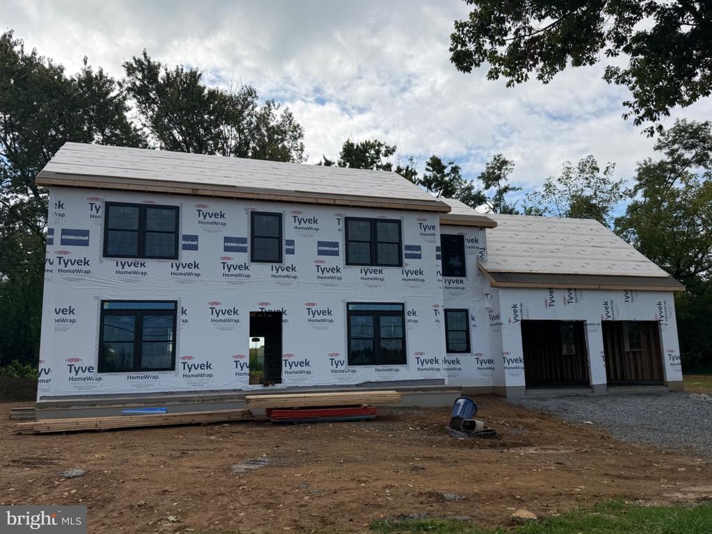 Two-story house under construction with Tyvek wrapping, dark-framed windows, and an attached garage.