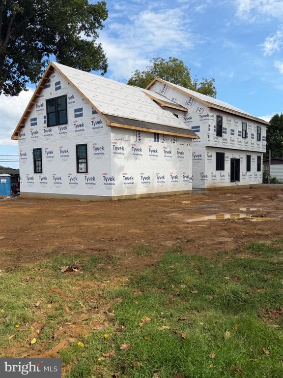 Two-story house under construction, wrapped in Tyvek with windows installed and roof partially shingled.