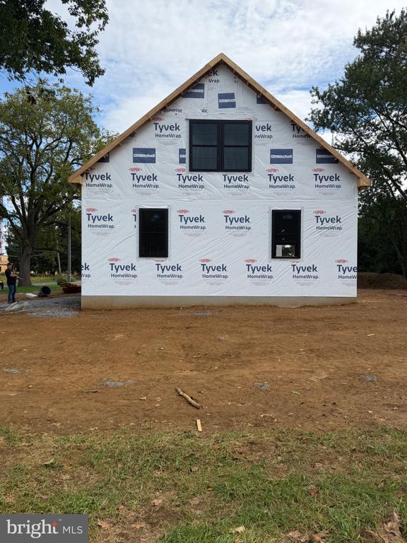 House under construction wrapped in Tyvek, with installed windows and an unfinished dirt yard.