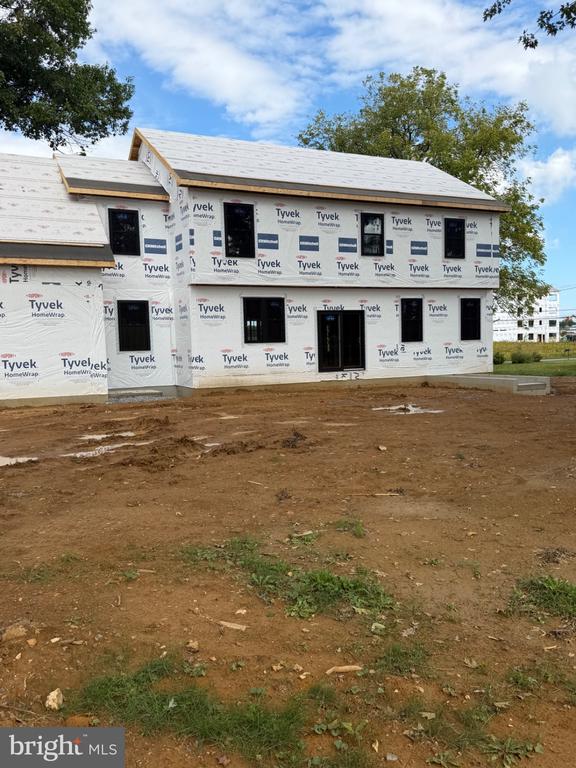 Two-story house under construction, wrapped in Tyvek, with an unfinished dirt yard.
