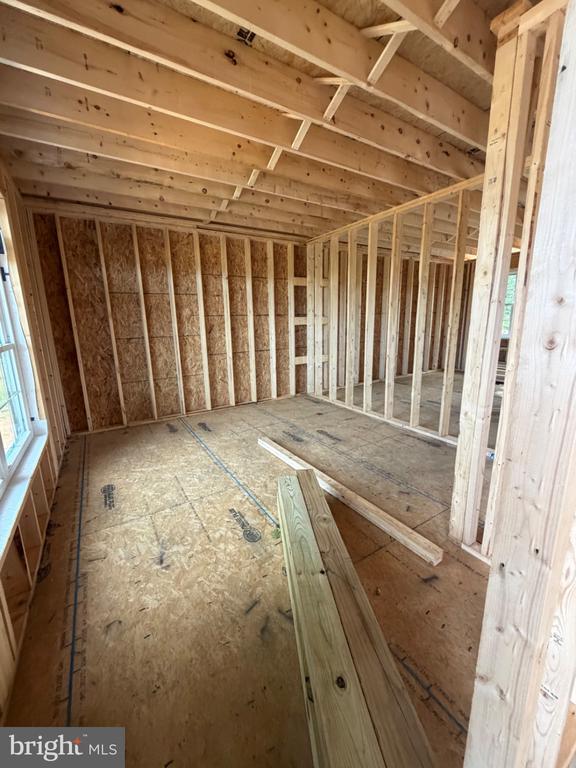 Unfinished interior room with exposed wood framing, roof trusses, and plywood subfloor.
