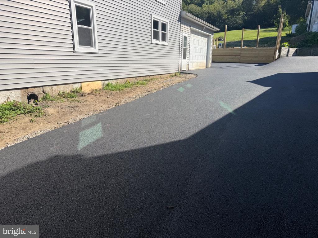 Paved driveway beside a gray-sided house and attached garage, with a wooden retaining wall at the far end.