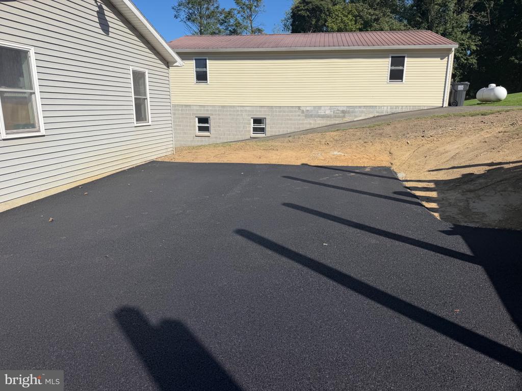 House exterior with a red metal roof beside a newly paved driveway and graded dirt.