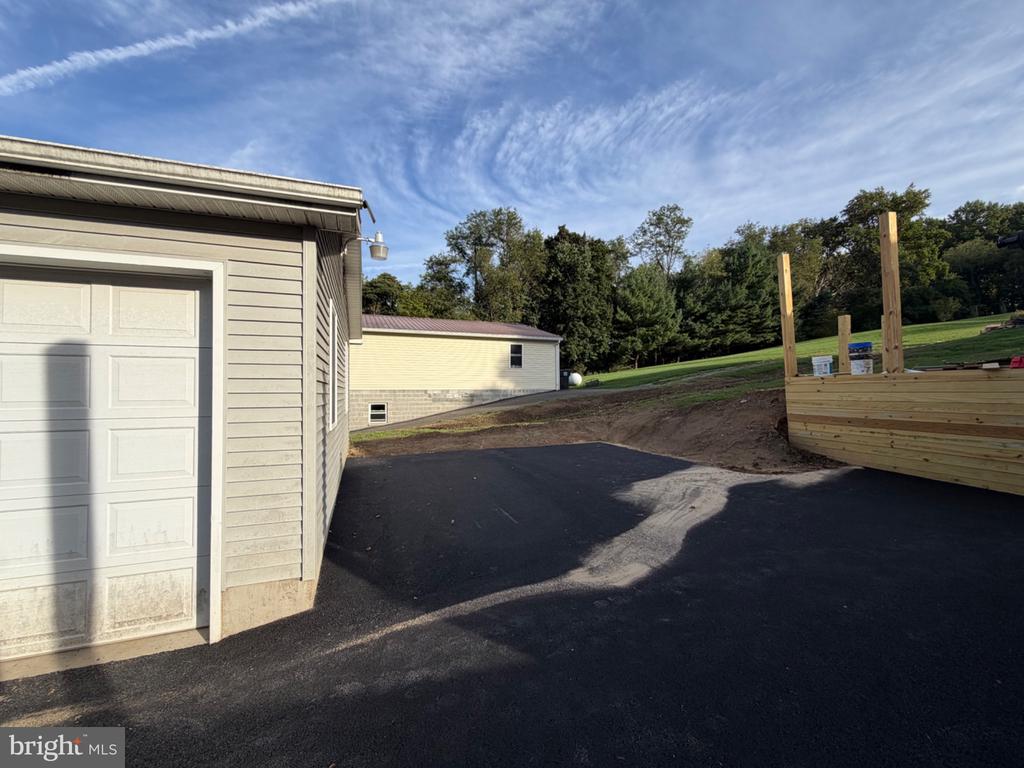 Garage beside a newly paved driveway, with a wooden structure under construction along the edge.