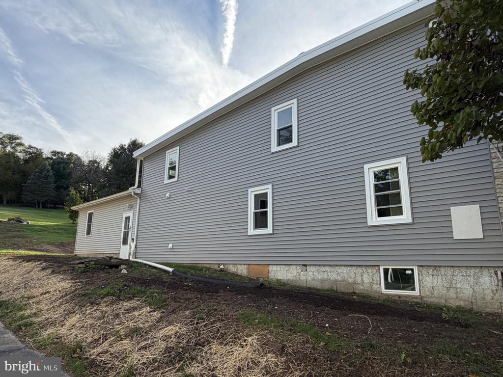 Gray-sided two-story house with white-trimmed windows and bare ground beside the foundation.