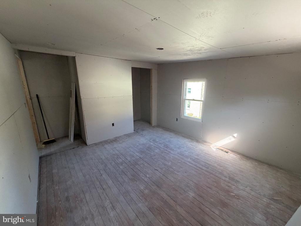 Unfinished interior room with bare wood plank flooring, drywall, a window, and an open doorway.