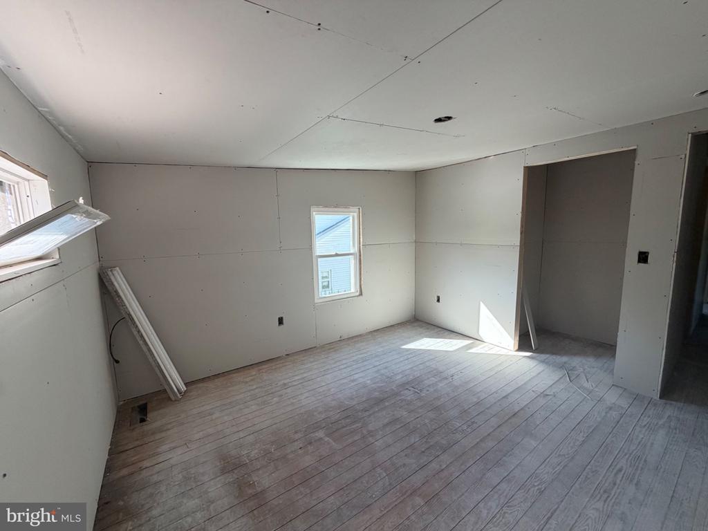 Unfinished interior room with drywall, bare plank flooring, two windows, and an open doorway.