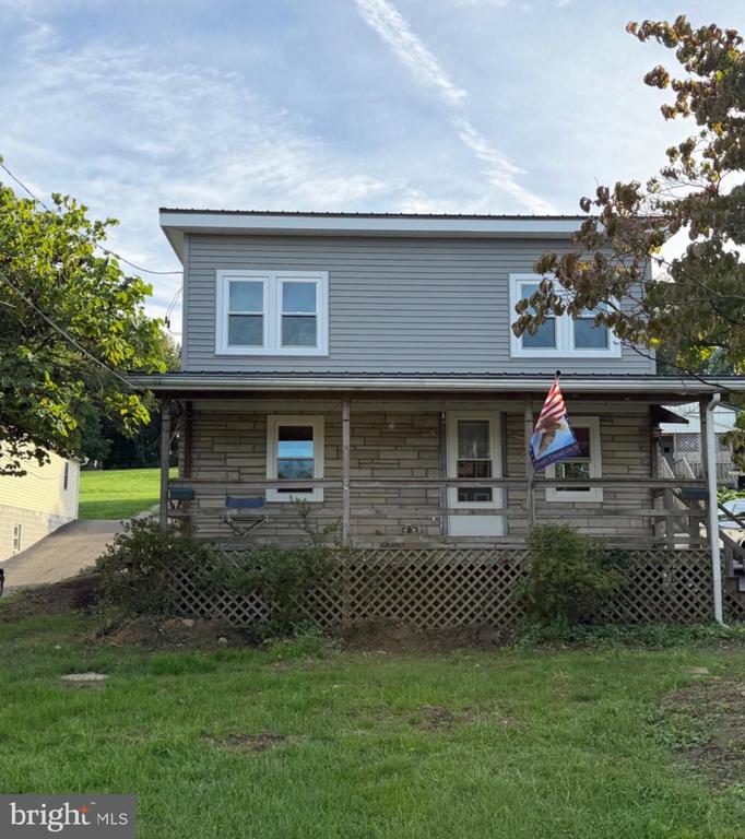 Two-story gray and stone house with a wide covered porch, lattice skirting, and an American flag.